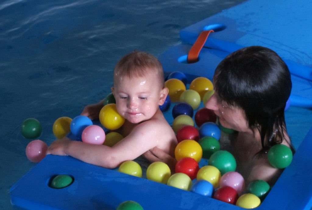 matka s dítětem v bazénu s balónky a plovoucími deskami